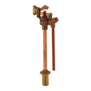An antique brass yard hydrant with a long copper pipe and a red handle.