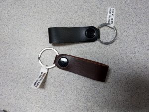 Two leather keychains with metal rings on a speckled surface, one black and one brown, with labels.
