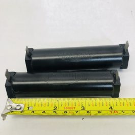 Two black cylindrical machine parts with brand imprint alongside a measuring tape.